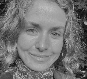 A black and white photo of the face of a young woman with shoulder-length blonde hair. She is smiling and looking directly at the camera.