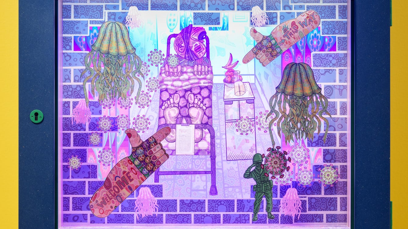 Photograph of a diorama called The Fruit and the Pee. A bowl of fruit is on a table beside a figure in a bed with floating jellyfish and two arms in the upper right and lower left hand corner pointing towards the bowl of fruit.