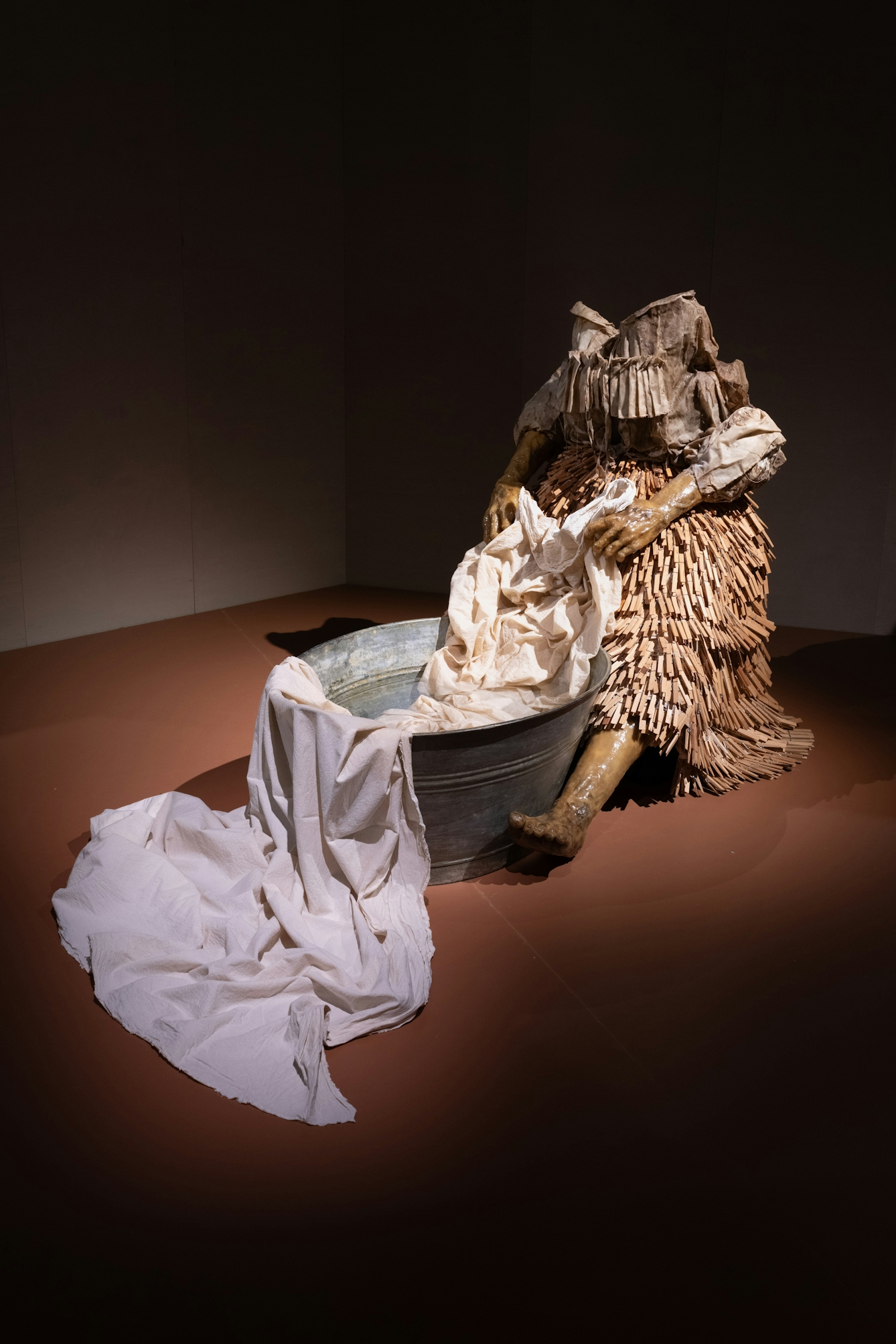 A photograph of a sculptural installation called washerwoman, the sculpture is made of beeswax, resin and brown cloth and is adorned with wooden clothes pegs.