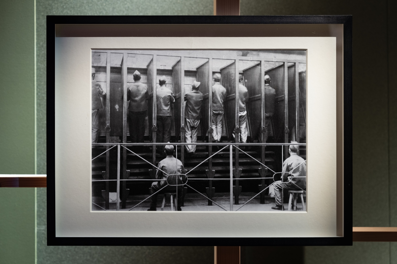 A photograph of a framed black and white photographic print depicting prisoners on a treadmill being watched by prison guards.