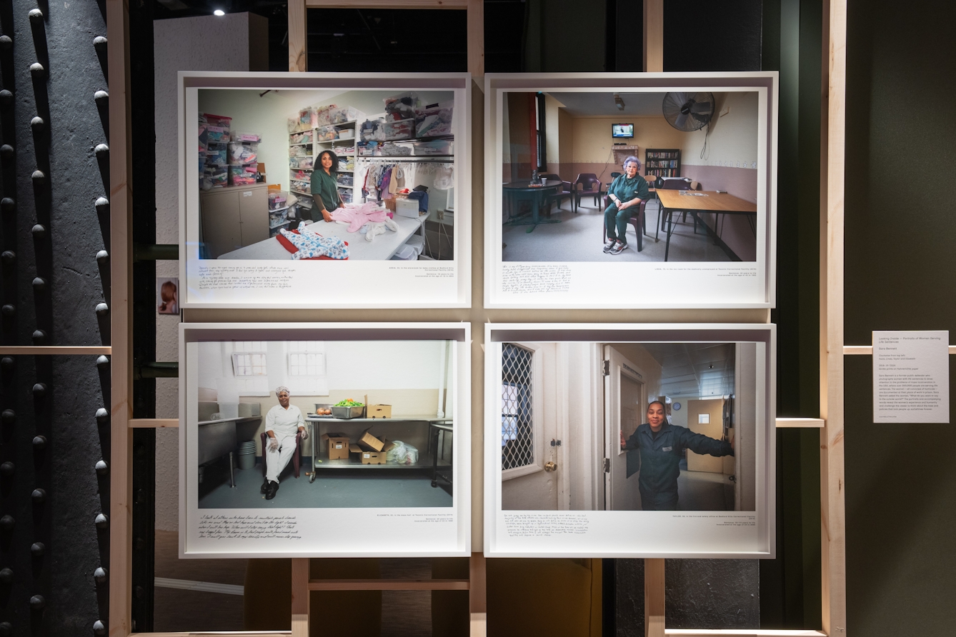 A photograph showing four photographic prints depicting portraits of incarcerated women displayed in white frames, against a background of wooden slats.