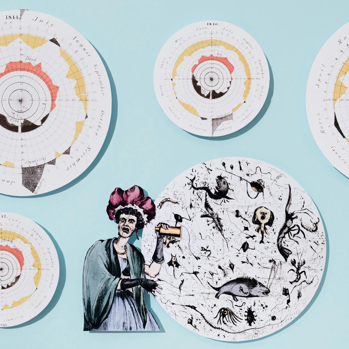 Photograph of cut out pieces of archive material from above, all raised slightly above a flat light blue background. One of the illustrations shows a shocked woman looking at enlarged microscope illustration of caricatured microbes found the dirty water causing a cholera outbreak. Surrounding the woman is a series of circular illustrations showing infection rates of the cholera outbreak during different years starting in 1840.