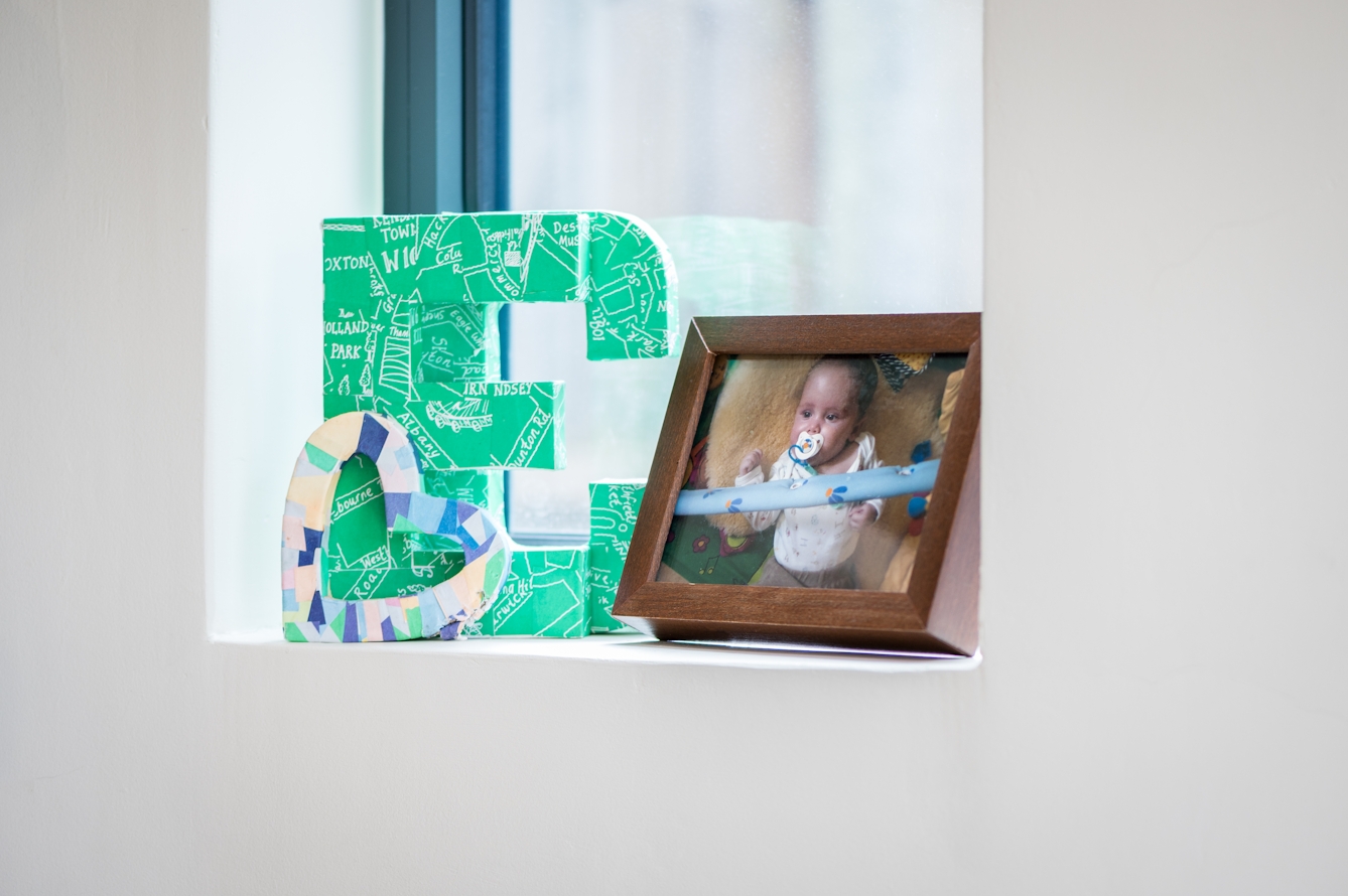 Photograph showing a window recess containing an ornamental letter E and C, and a small heart shape. There is also a framed photograph of a baby lying on the floor.