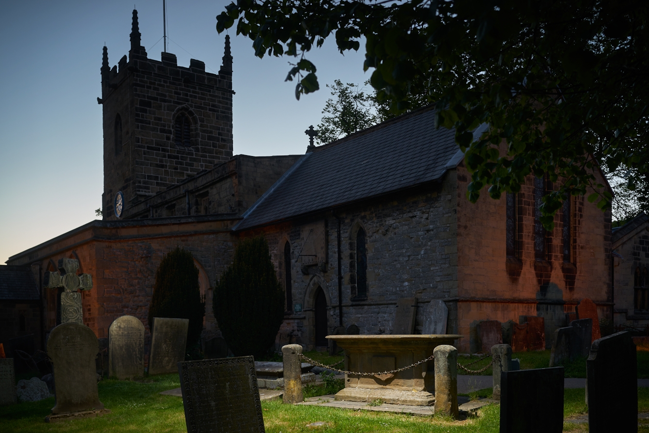 Photograph of a church and church yard at dusk. in the foreground the grave of Catherine Mompesson, wife of the rector, is spotlit.