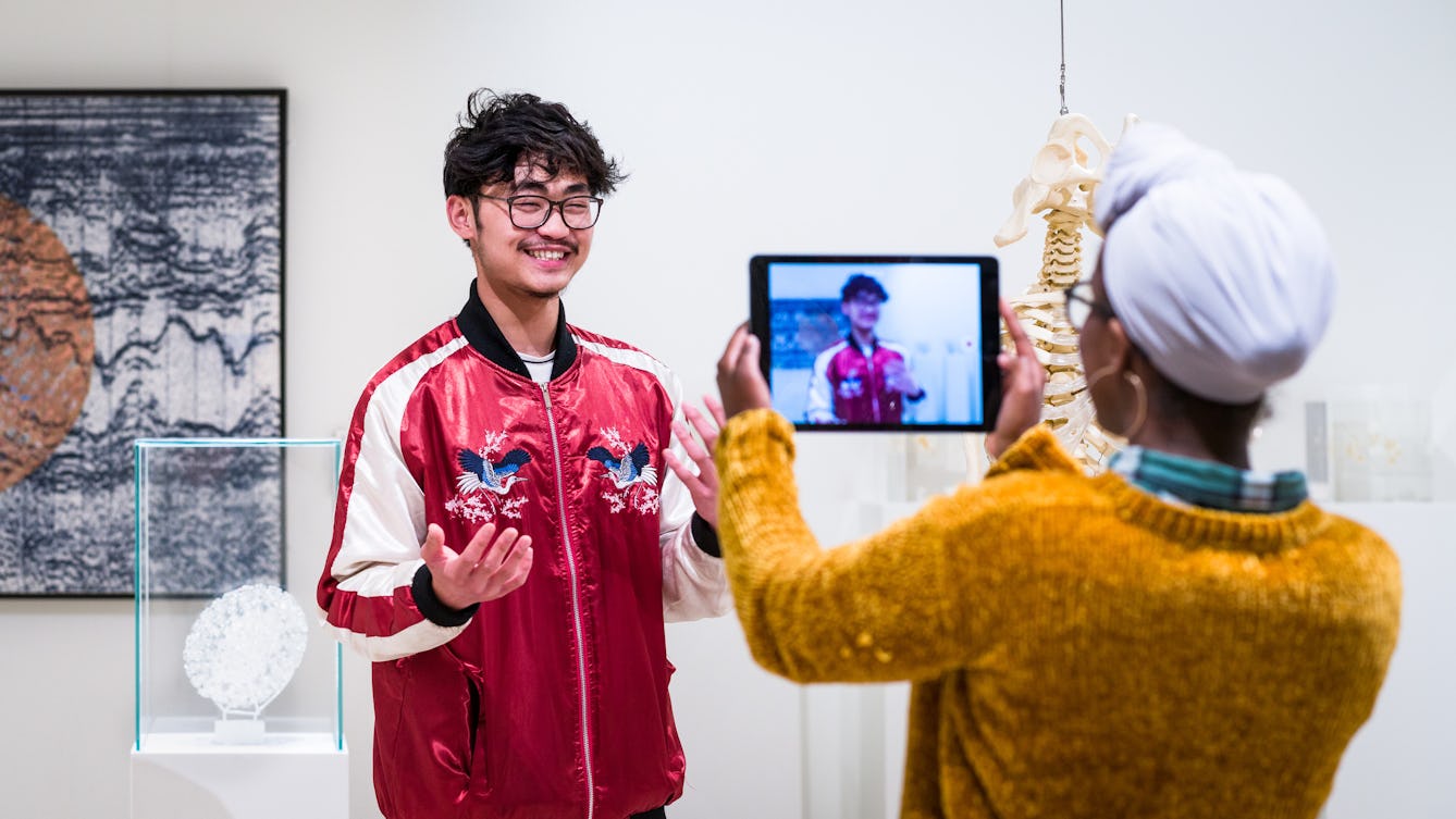 Photograph of a young man and woman using an iPad in the Medicine Man gallery to film each other talking to camera.