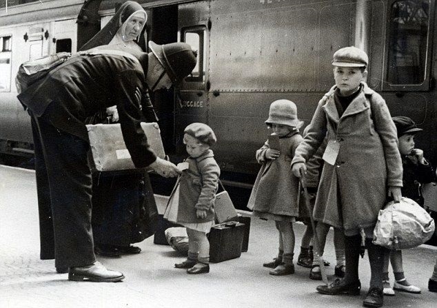Children stand on a station platform, with labels attached to their coats.
