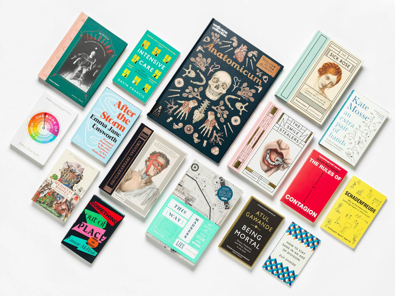 Photograph of 16 books lying flat on their backs arranged in a loose grid on the diagonal. The covers range in colour and design. They have been photographed on a white background with a small grounding shadow.