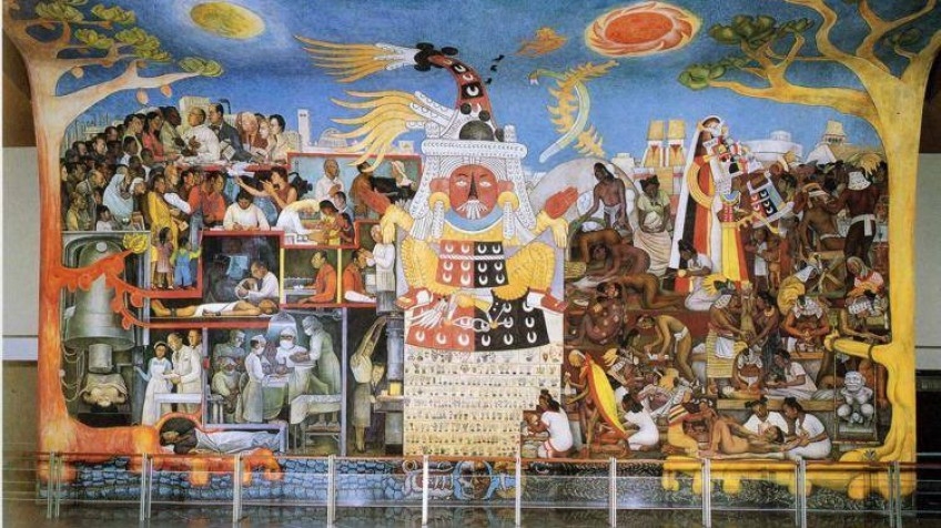 Colour photograph of a mural featuring many people and healthcare workers. The Mesoamerican goddess Tlazoltéotl is at the centre of the image, with two tall trees either side. The sun and the moon are visible in a bright blue sky.