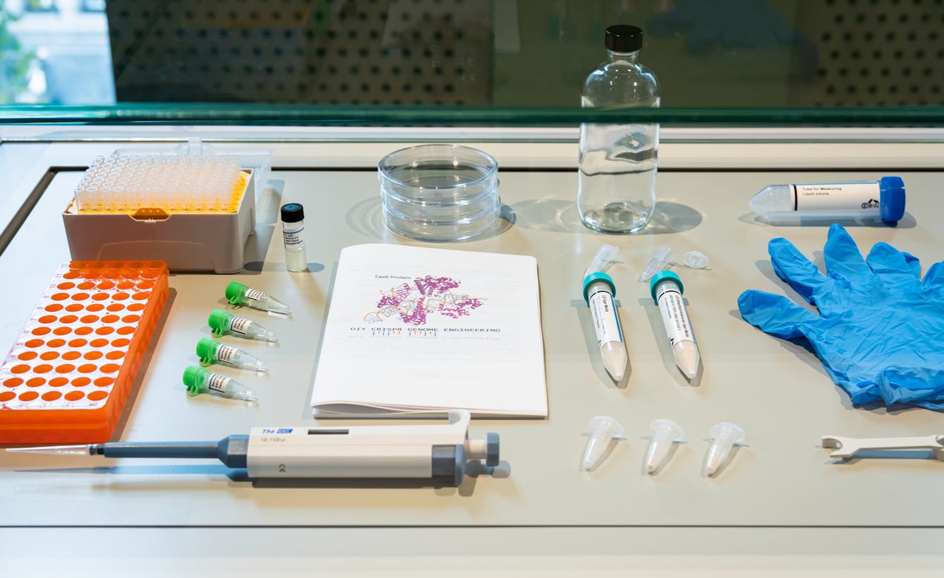 Photograph of the contents of an exhibition display case. The objects on display include a scientific pipet, petri dishes, latex gloves, specimen tubes and a jar.