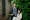 Photograph of a young woman and a mother figure in a domestic garden. The young woman is seated in a long dress and and the mother figure stands behind her, hand on her shoulder. They are both looking to camera.