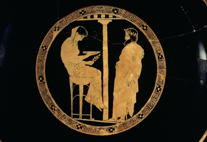 Black and gold decorated bowl depicting a woman seated on a stool gazing into a bowl as a man stands before her waiting.