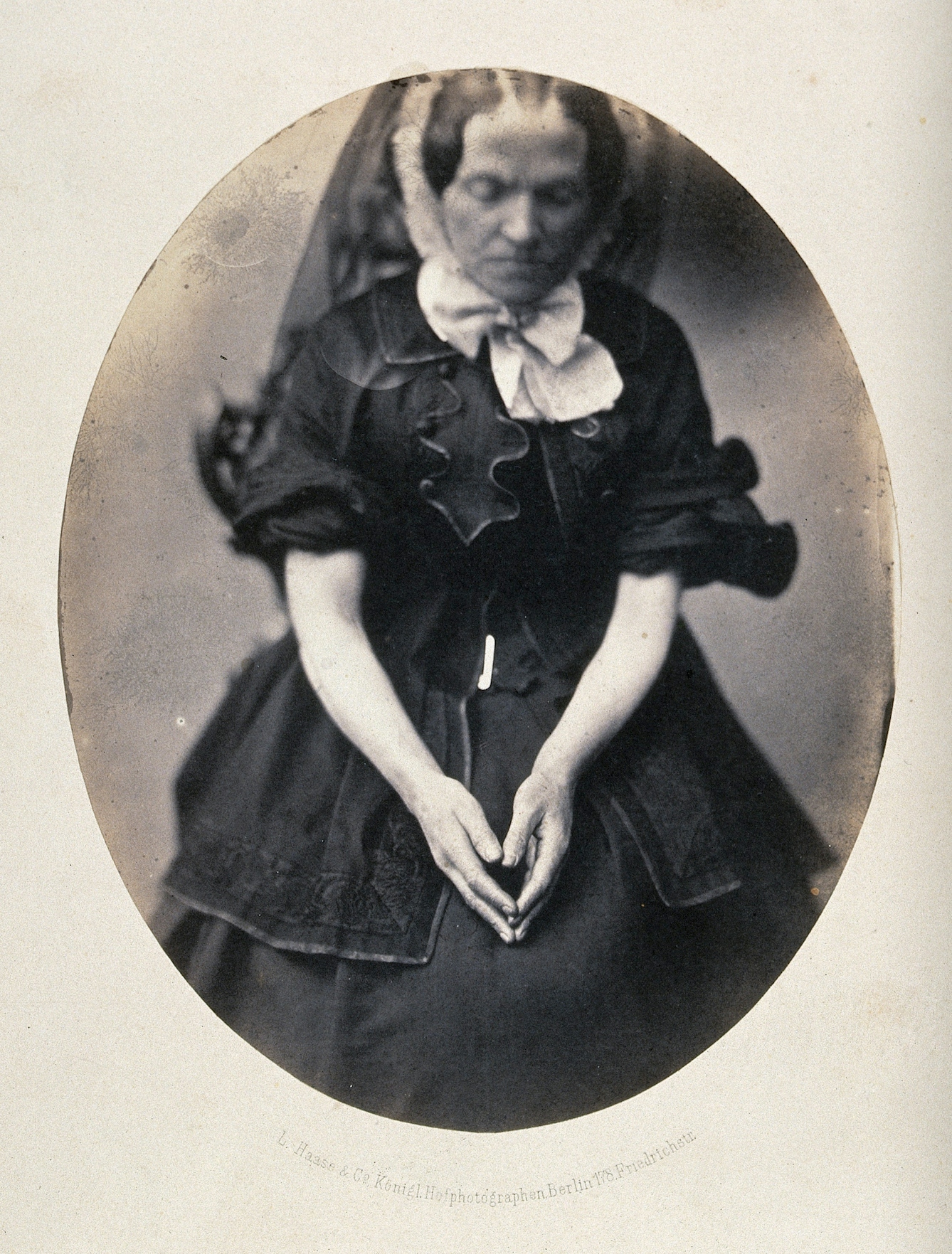 Photograph of a woman, seated, wearing a black dress and veil