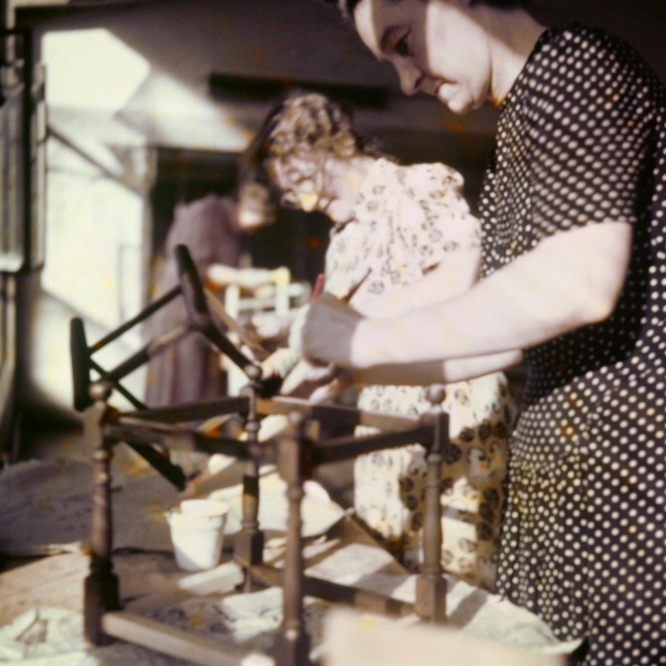 Photograph from the mid-20th Century Peckham Pioneer Centre, showing three women who appear to be assembling and staining some sort of wooden furniture, possibly the bottom of a chair.