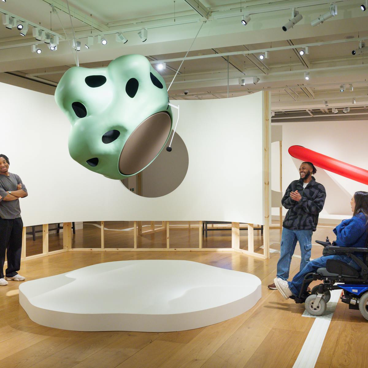 A view of four people looking at a large sculptural installation of noses. In the background is a large inflatable red arm