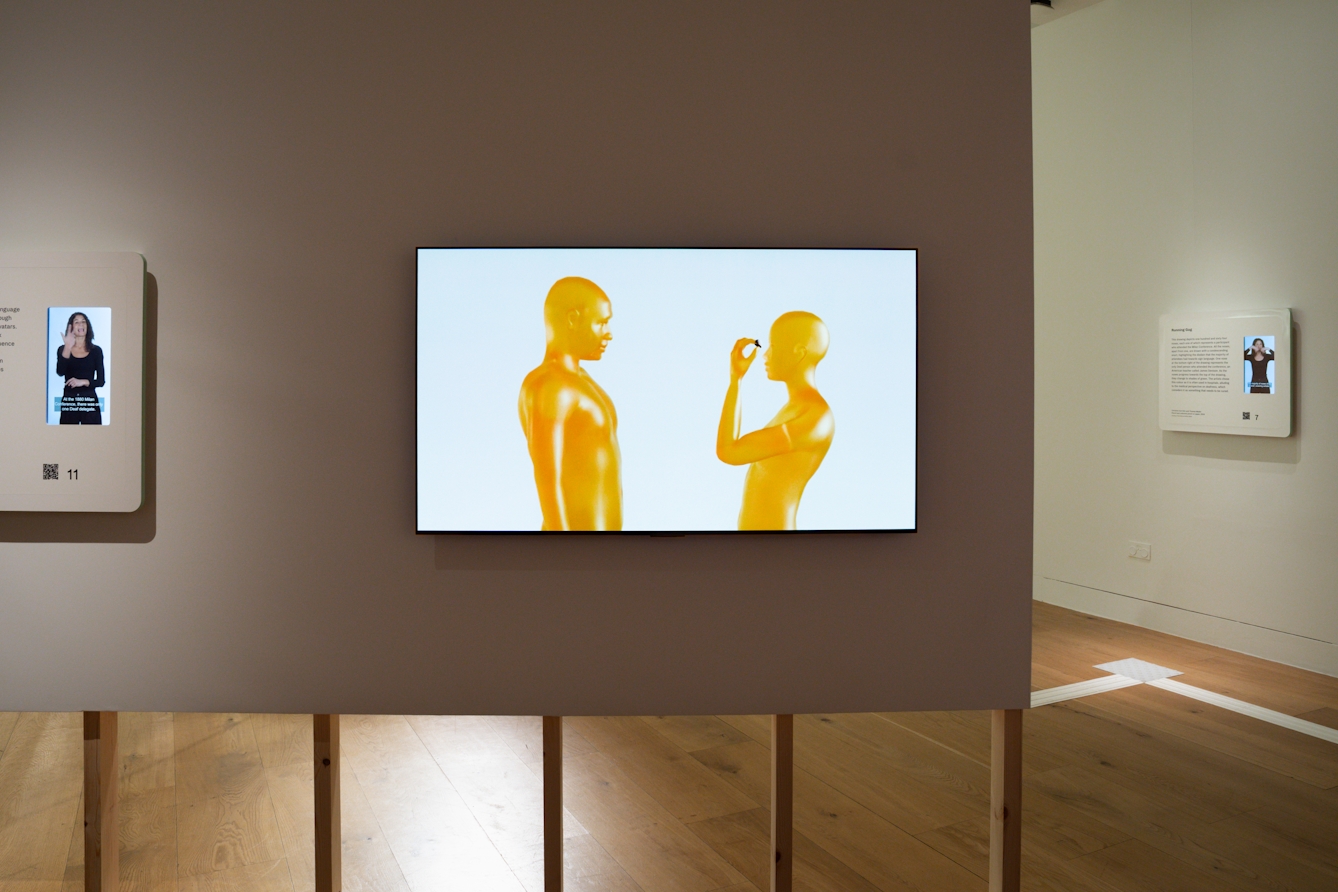 A photograph of a video installation featuring two animated yellow figures, passing each other their eyes.
