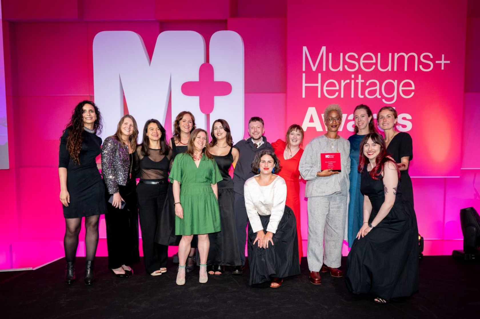 A group of people smiling to camera against the backdrop of the Museums+ Heritage Awards holding their Visitor Accessibility Award.