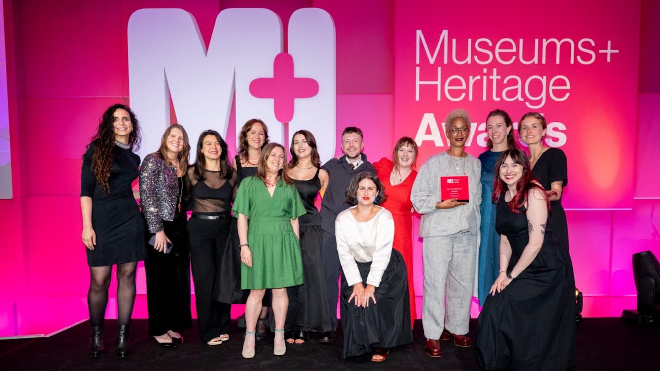 A group of people smiling to camera against the backdrop of the Museums+ Heritage Awards holding their Visitor Accessibility Award.