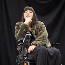 A photograph of Kyla who has short, dark hair and is wearing a green jacket, sitting in a wheelchair.