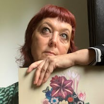 A photo of Sarah Jarrett holding a piece of her art. Sarah has red hair and wears a green shirt.