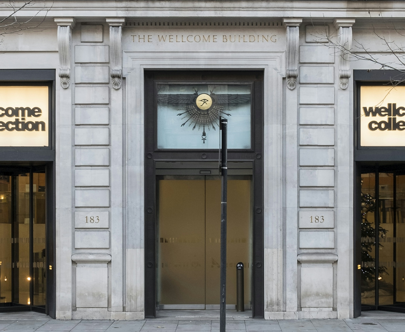 A large doorway in the facade of a white stone neo-classical building, featuring narrow pillasters on either side, supporting a lintel.