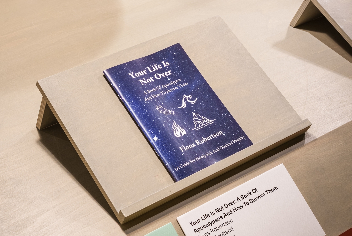 The zine 'Your life is not over' by Fiona Robertson, resting on a plinth in the gallery.