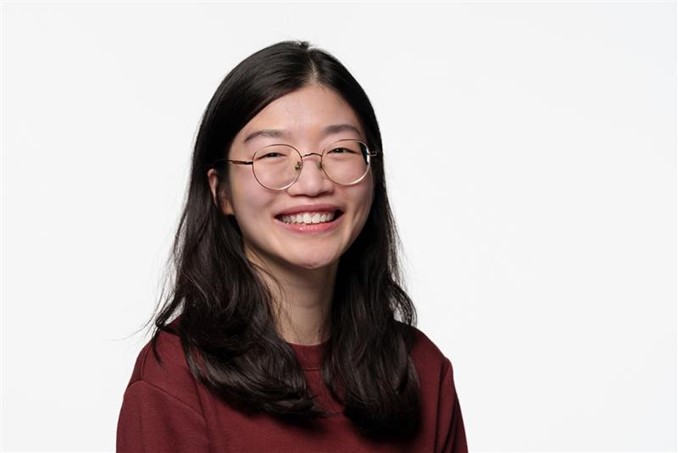 A headshot of Joelle smiling. Joelle has dark hari and wears glasses and a dark red jumper. 