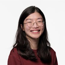 A headshot of Joelle smiling. Joelle has dark hari and wears glasses and a dark red jumper.