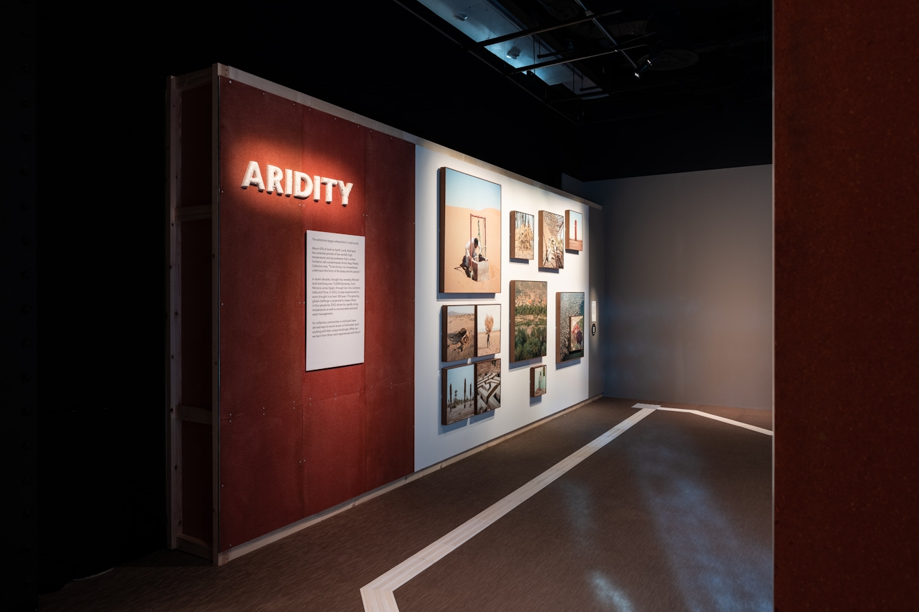 A large ceramic sign that reads 'Aridity' with a series of square photographs in the background.