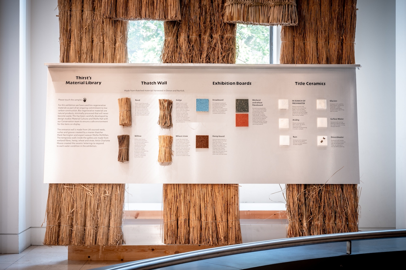 A wall covered in thatch with a display of plant-based materials used throughout the exhibition.