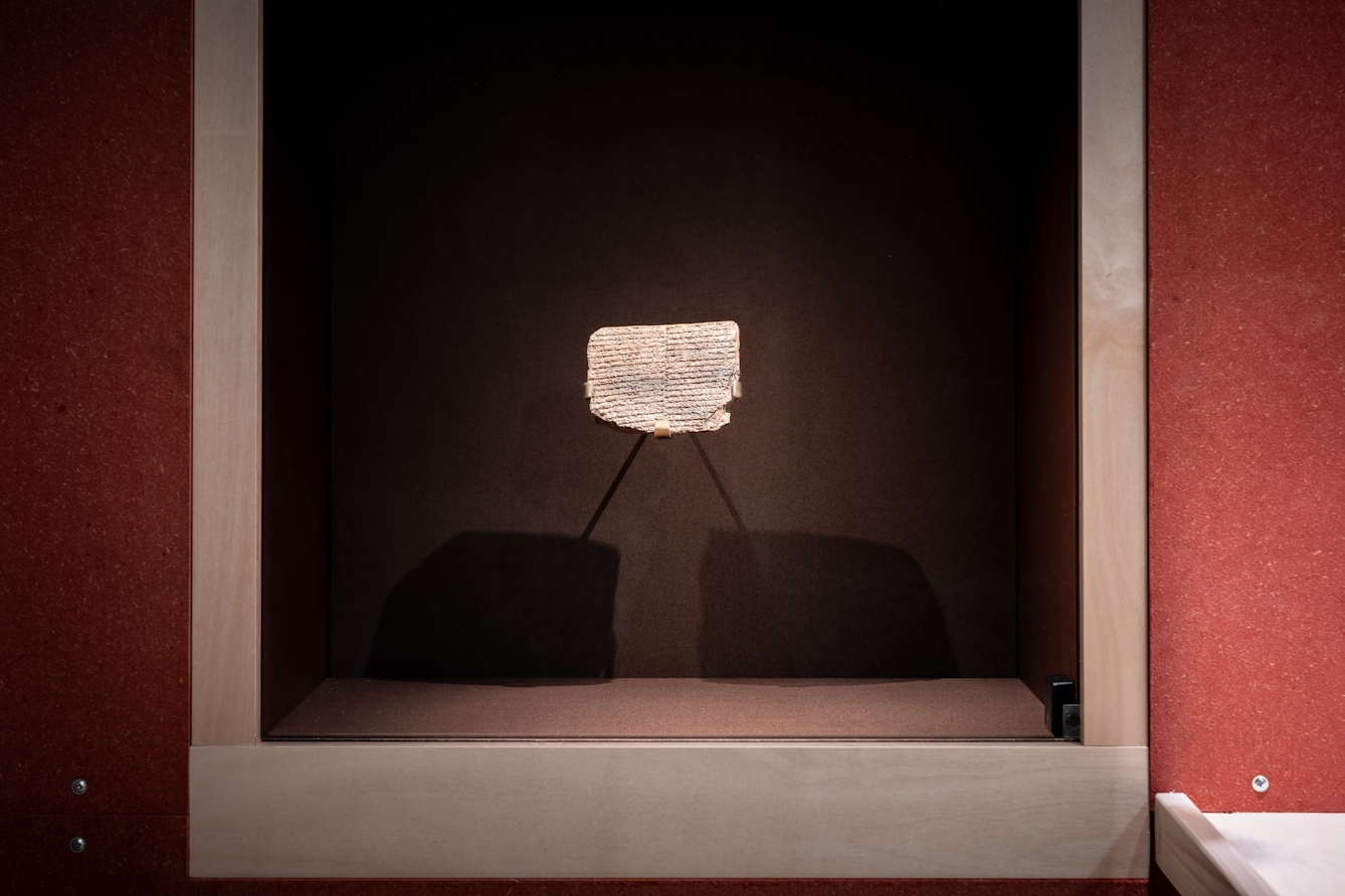 An segment of ancient clay tablet in a glass display case.
