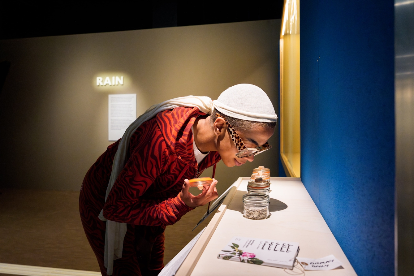 A person leabing over and smelling herbs in a glass jar.