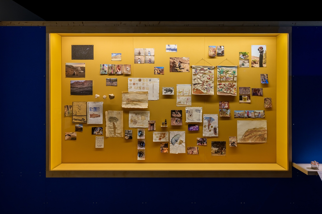 A wall of paintings, tapestries / embroideries and photographs.