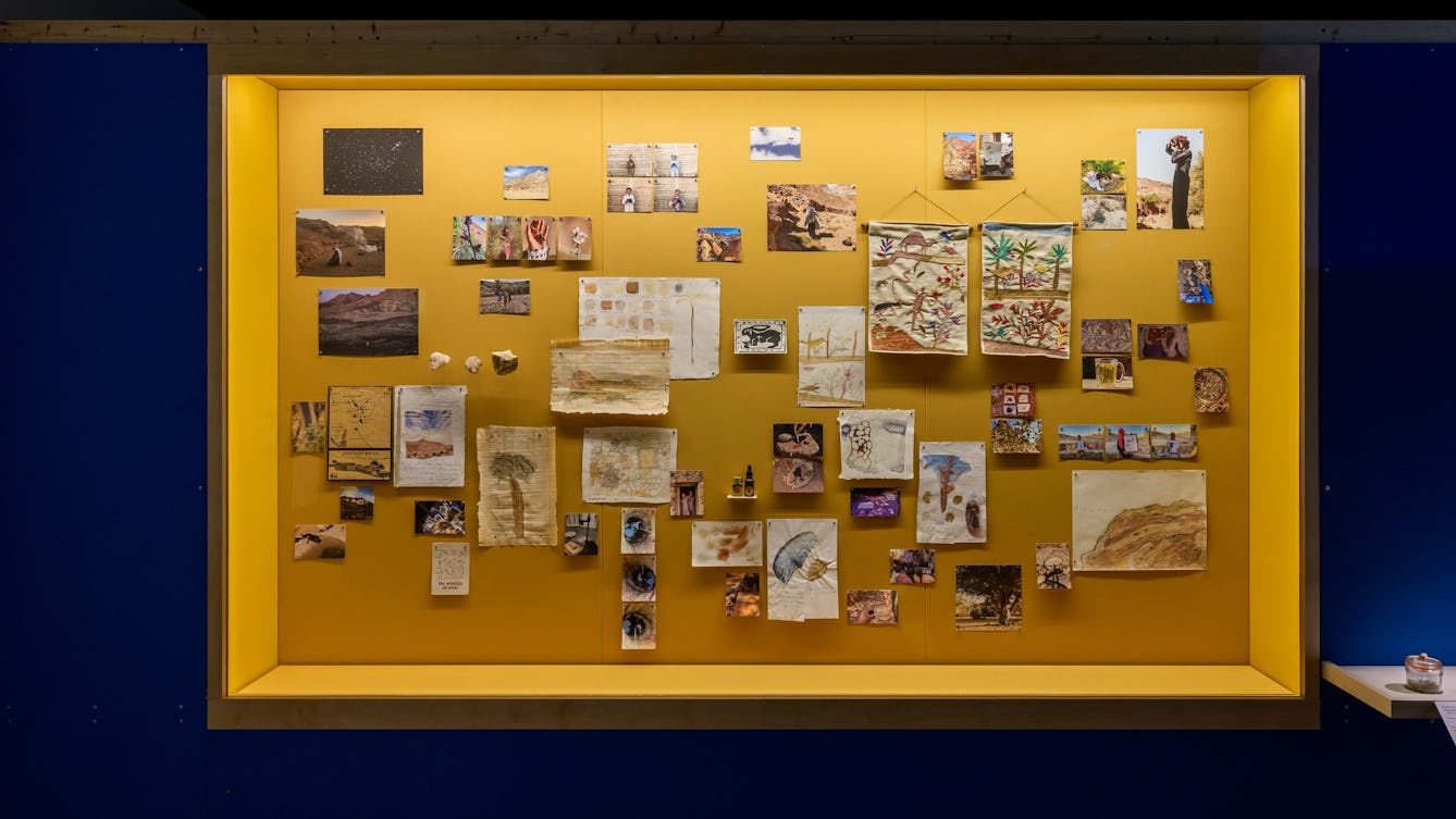 A wall of paintings, tapestries / embroideries and photographs.