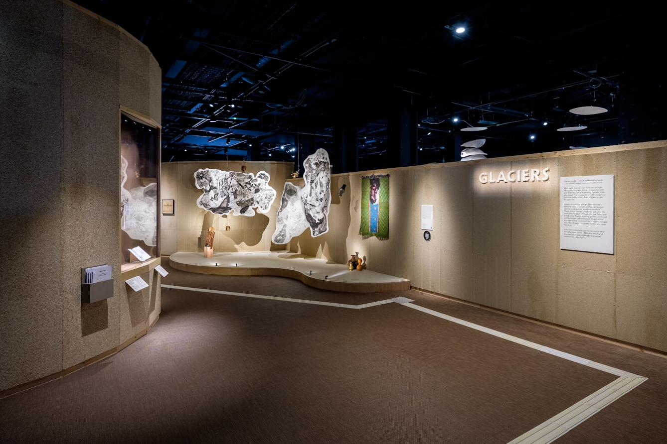 A large ceramic sign on a wall that reads 'Glaciers' with three hanging ink drawings on cotton paper in the background.