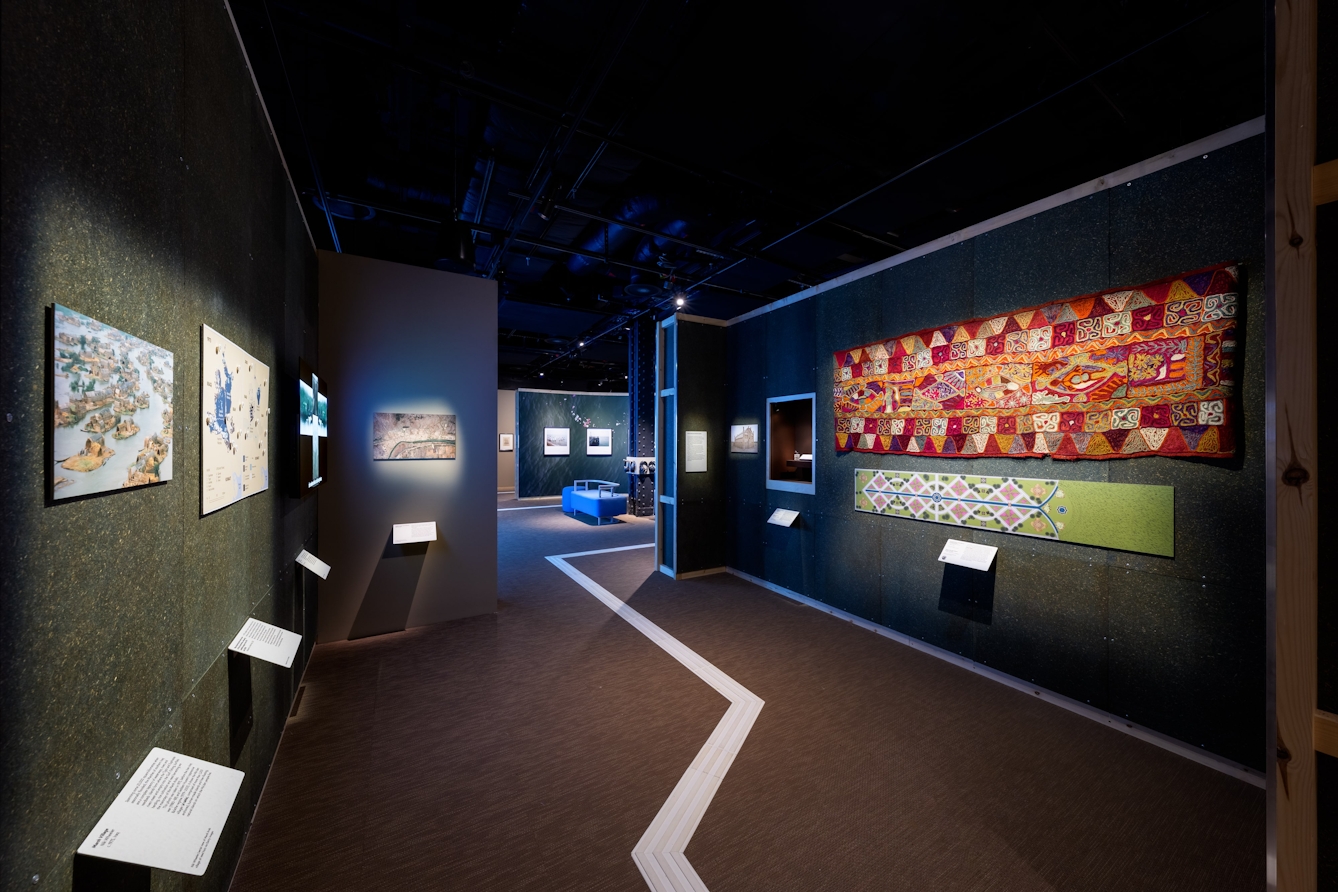 A display of photographs, maps, a wedding blanket, historical objects and a film work.