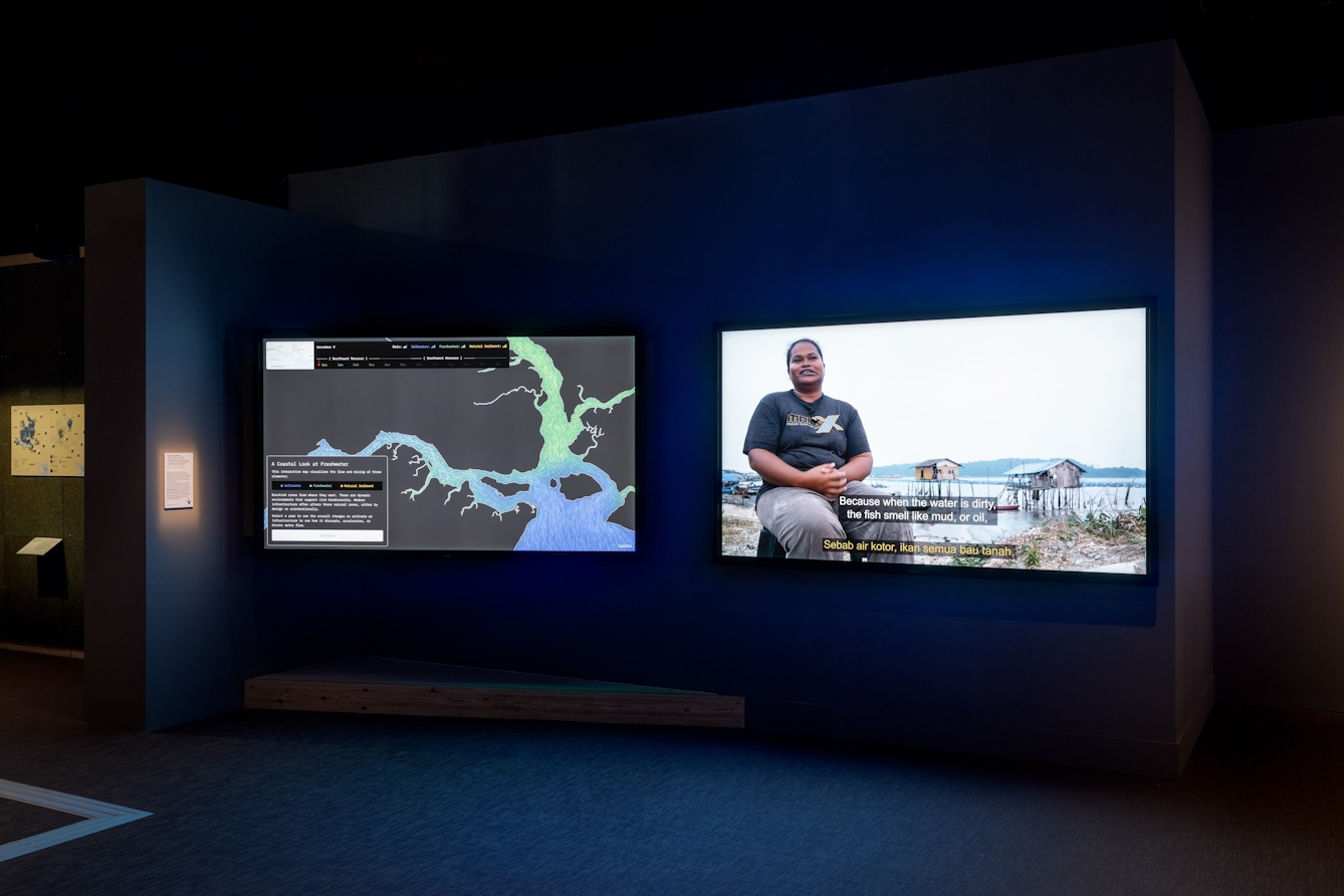Two adjacent, wall-mounted screens. One showing a film and the other an interactive map of waterways.