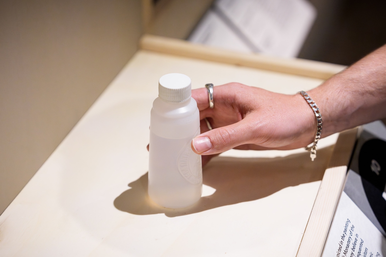 A hand touching a plastic bottle containing sacred water.