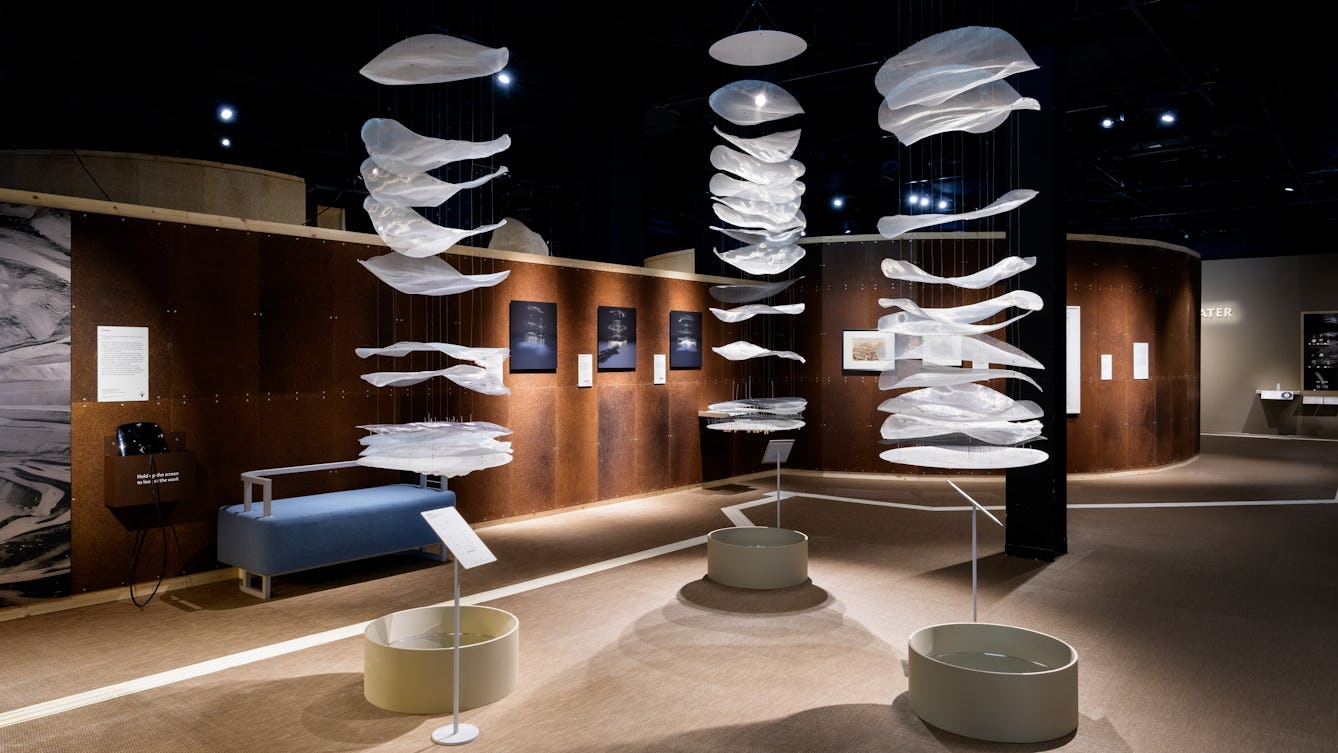 Three large sculptures suspended from the ceiling that show the different layers of water below the ground.