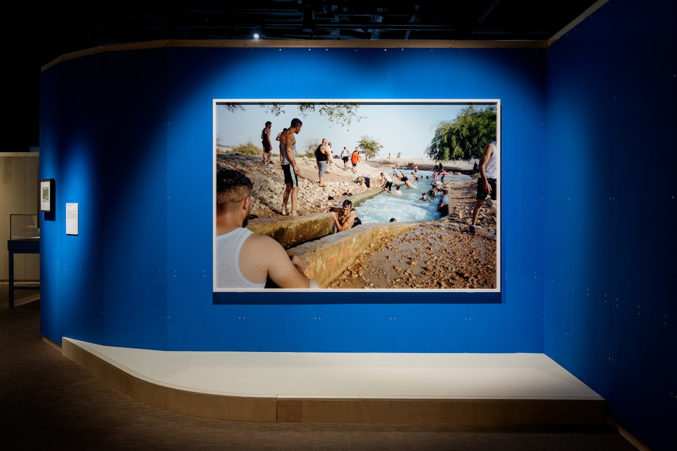 Large framed photographic print hanging on a blue wall. The shows men swiming and jumping into a constructed waterway.