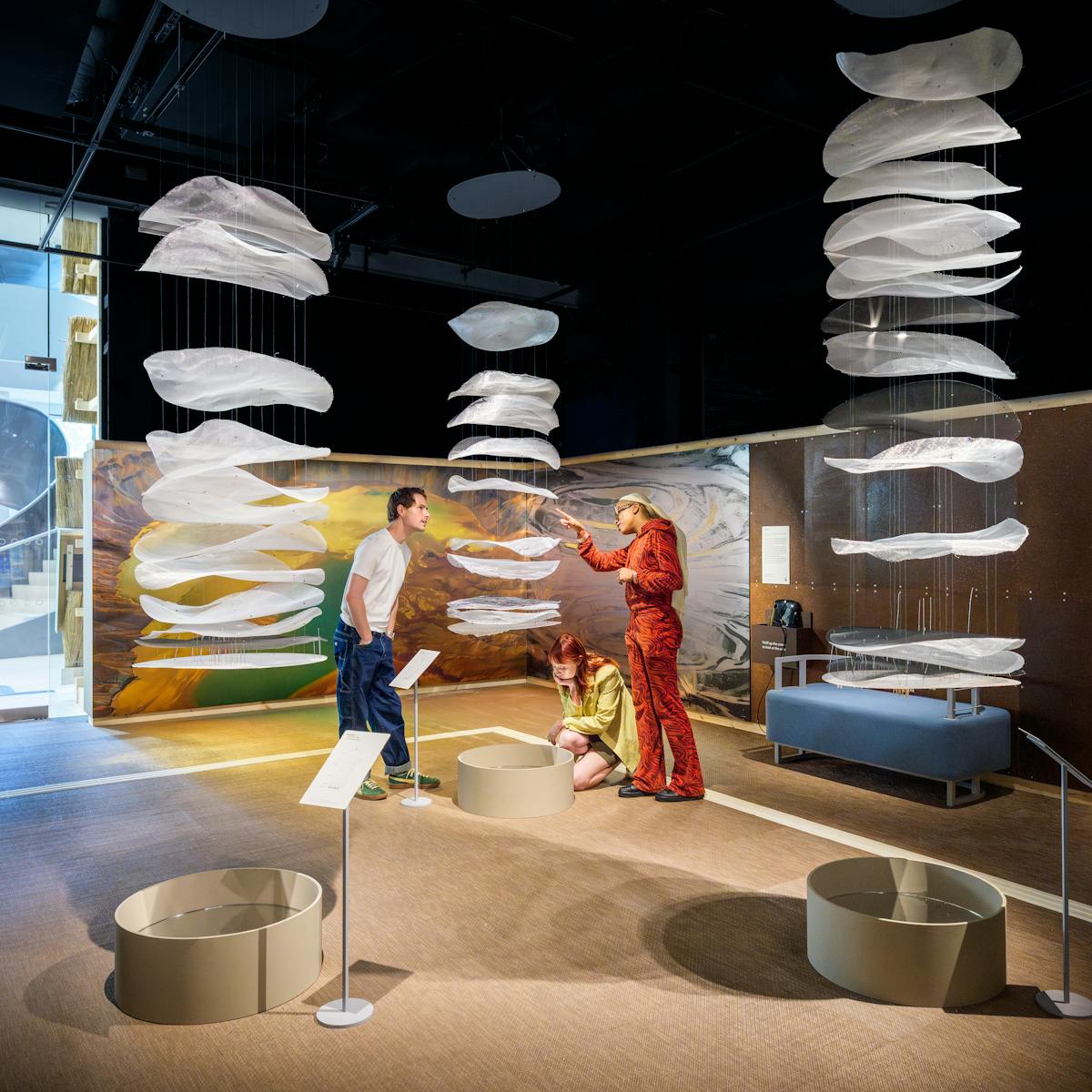 Three gallery visitors stand within a suspended sculpture, talking about the work.
