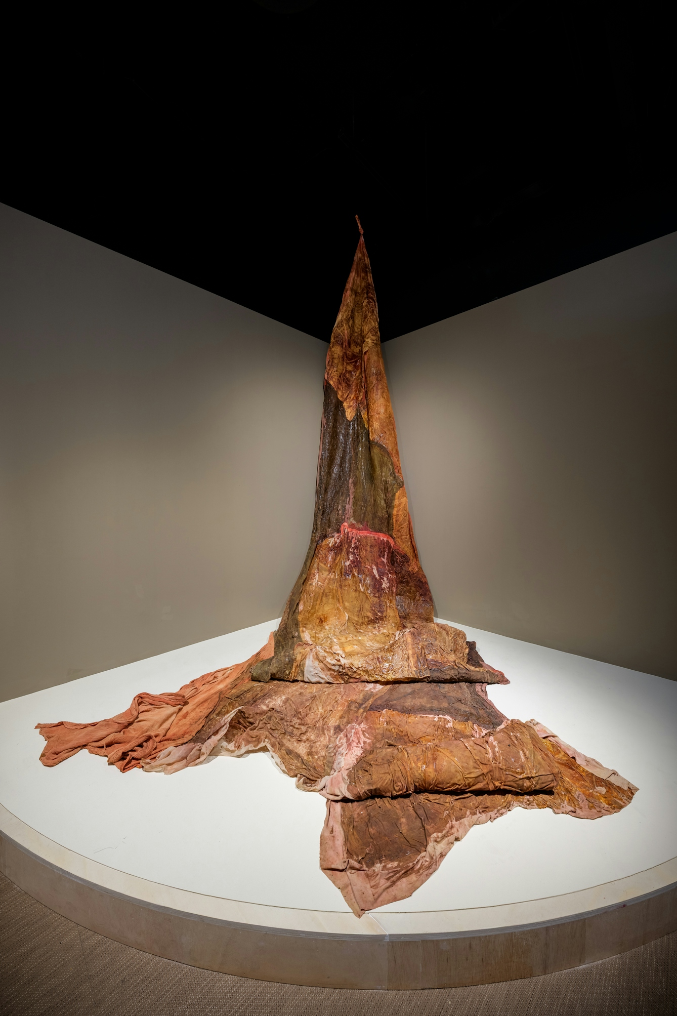 Photograph of a large mottled red and rust coloured material fabric cascading from the ceiling onto the gallery floor.