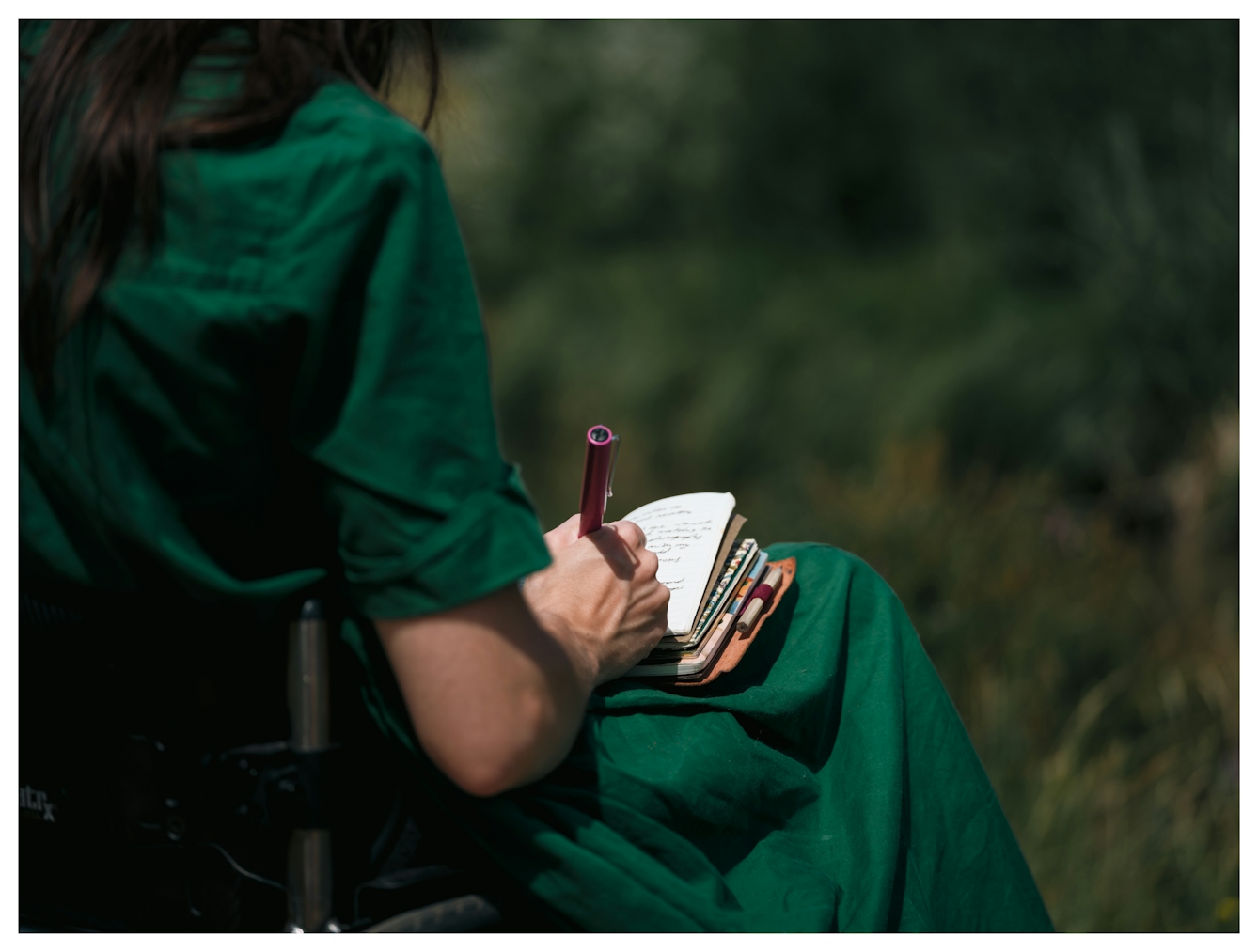 A close-up, over the shoulder view of a woman writing in a notebook resting on her lap.