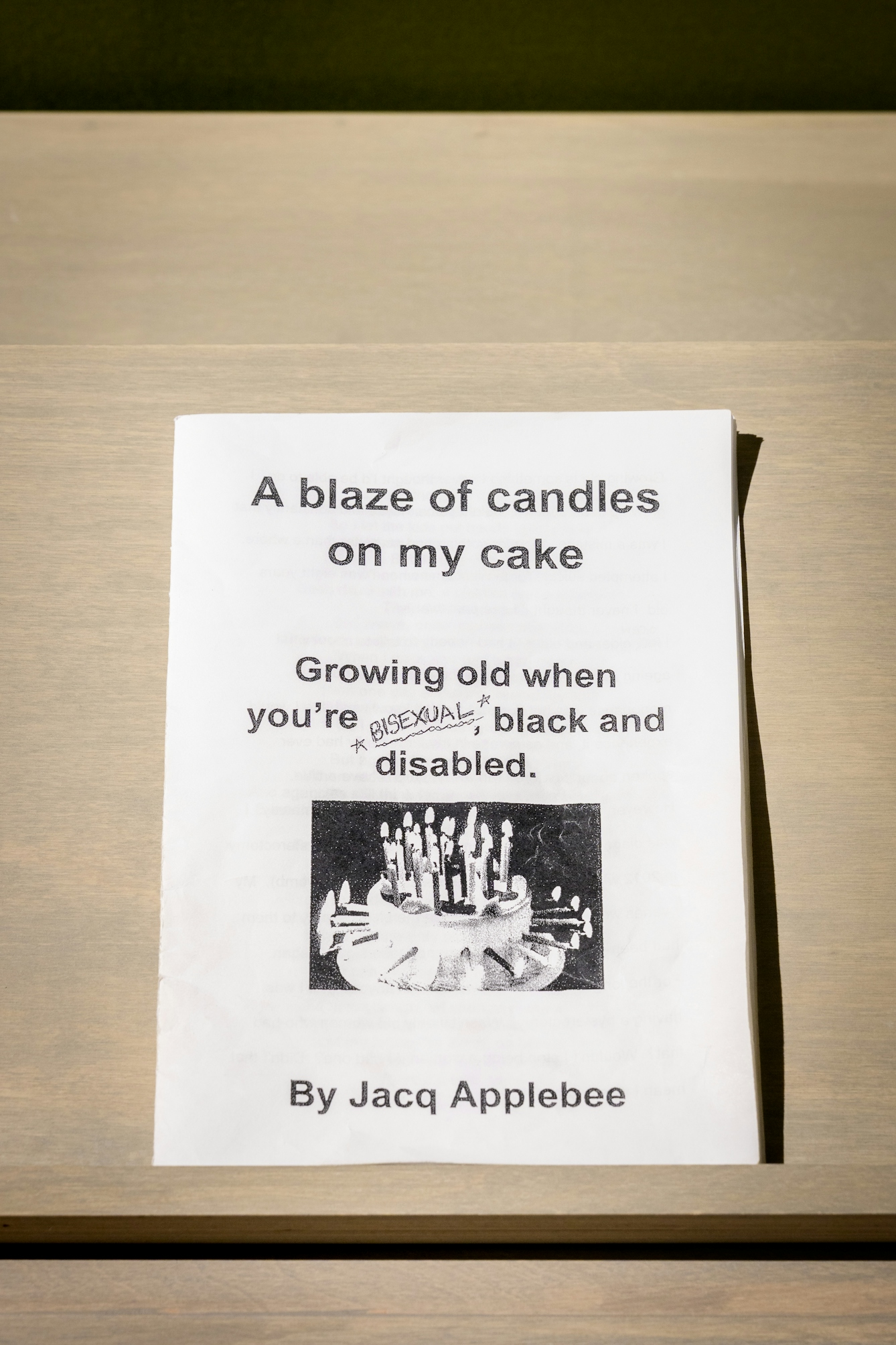 The zine 'A blaze of candles on my cake' by Jacq Applebee, resting on a plinth in the gallery.