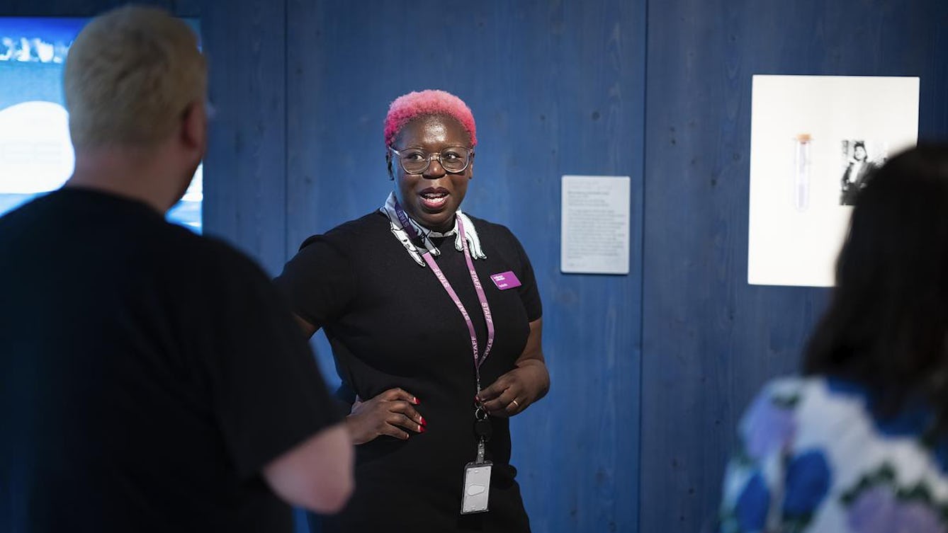 A facilitator with short, bright pink hair delivering a tour to a group of people.