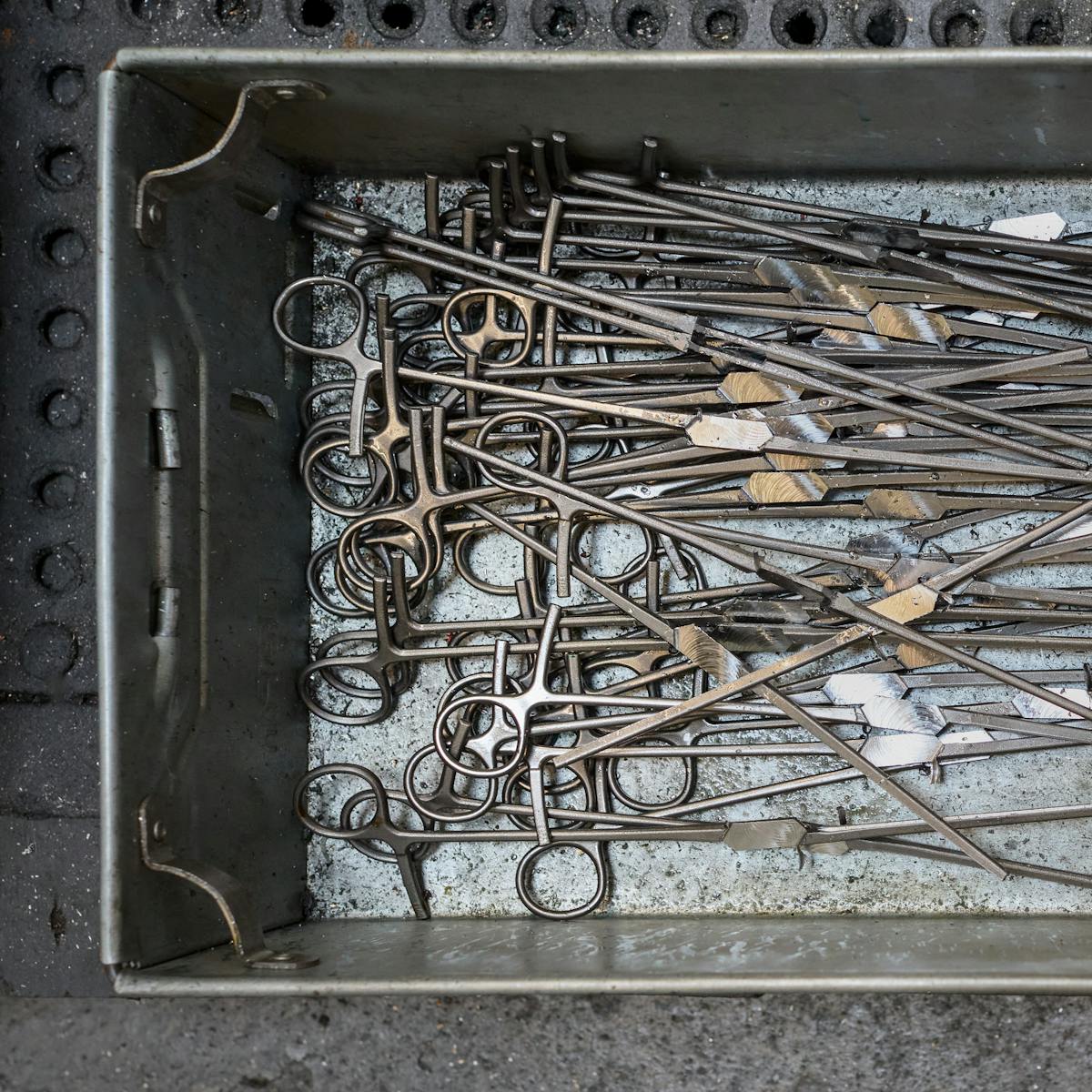Photograph of a metal industrial tray containing a pile of vascular clamp forgings at an early stage of manufacture.