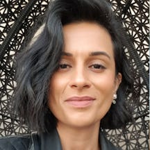 Photograph of the head and shoulders of a woman with short black hair with a blonde streak, leopard print top and leather jacket. She is looking and smiling directly at the camera.