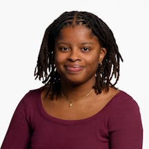 A headshot of Leona Letts smiling at the camera. She has shoulder-length dark hair and is wearing a maroon long-sleeved T-shirt, a gold pendant necklace, and small hoop earrings.
