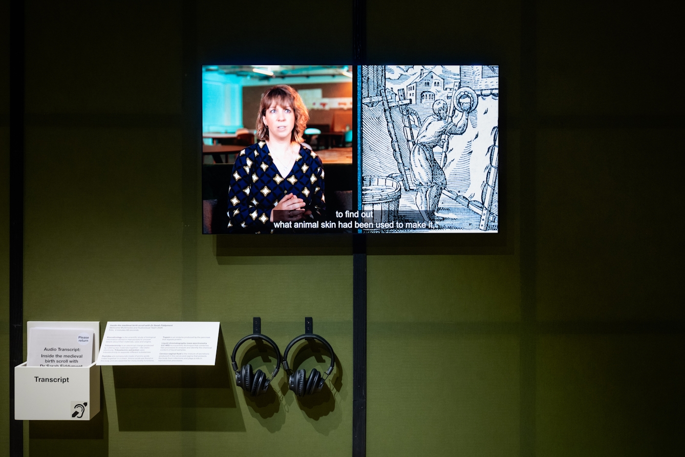 A tv screen showing a subtitled video of a woman talking and a page from a manuscript. Below which are headphones and written transcript.