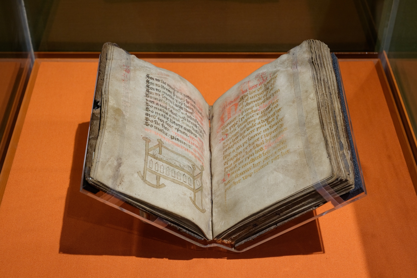 A manuscript in a display case, housed with supports. A line drawn illustration is visible on the open page.