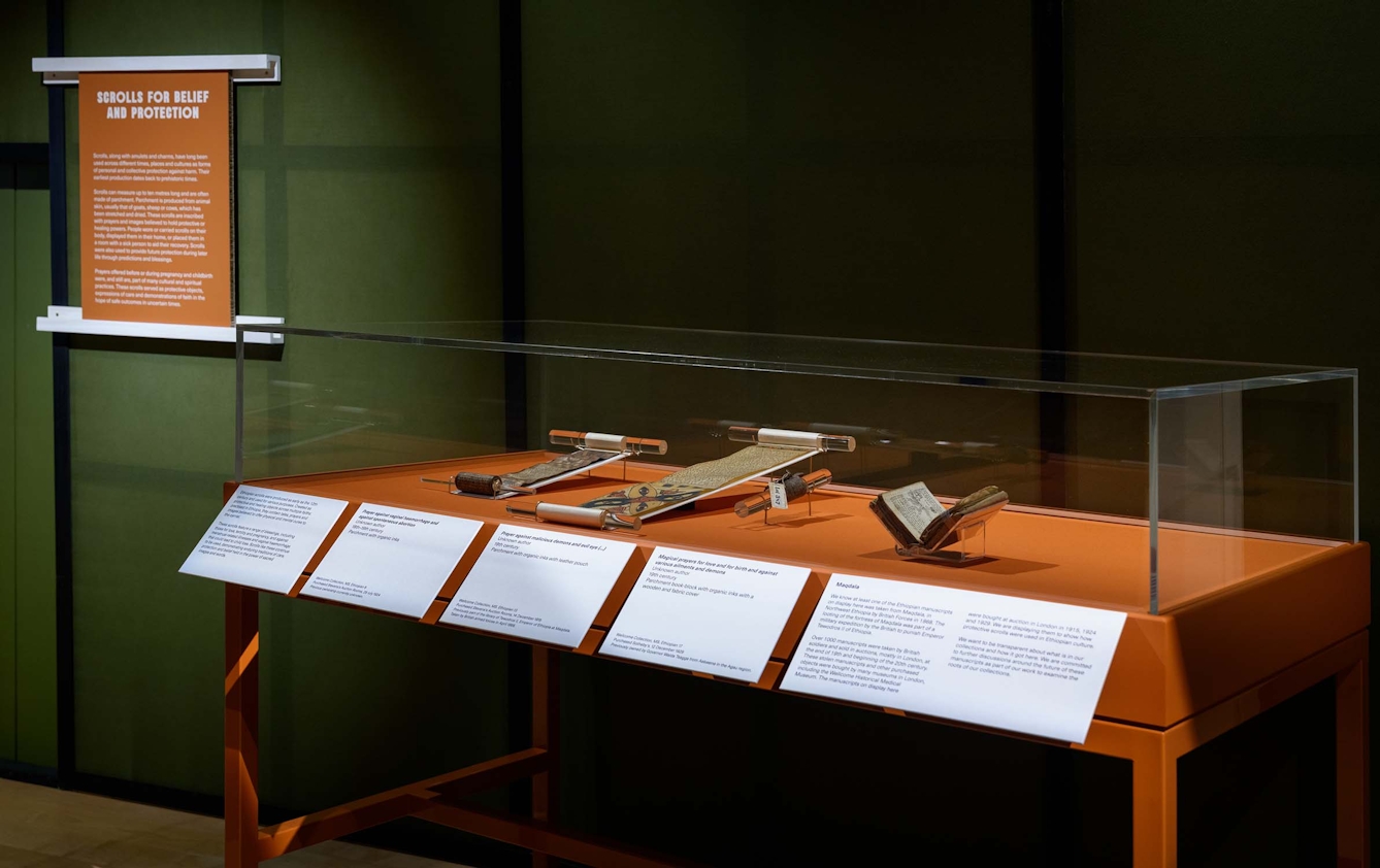 A museum display case showing two handwritten scrolls and a manuscript in book form.